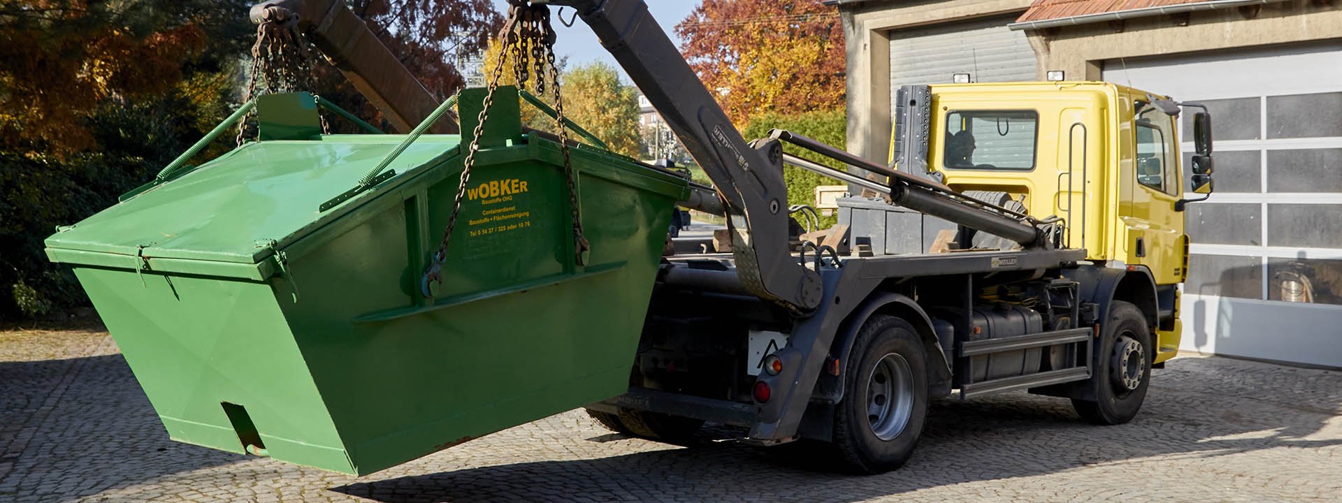 Gelber Lkw beim Verladen einer geschlossenen Mulde von Wobker Baustoffe e.K. in Melle f&uuml;r Entsorgung und Baustelleneinsatz